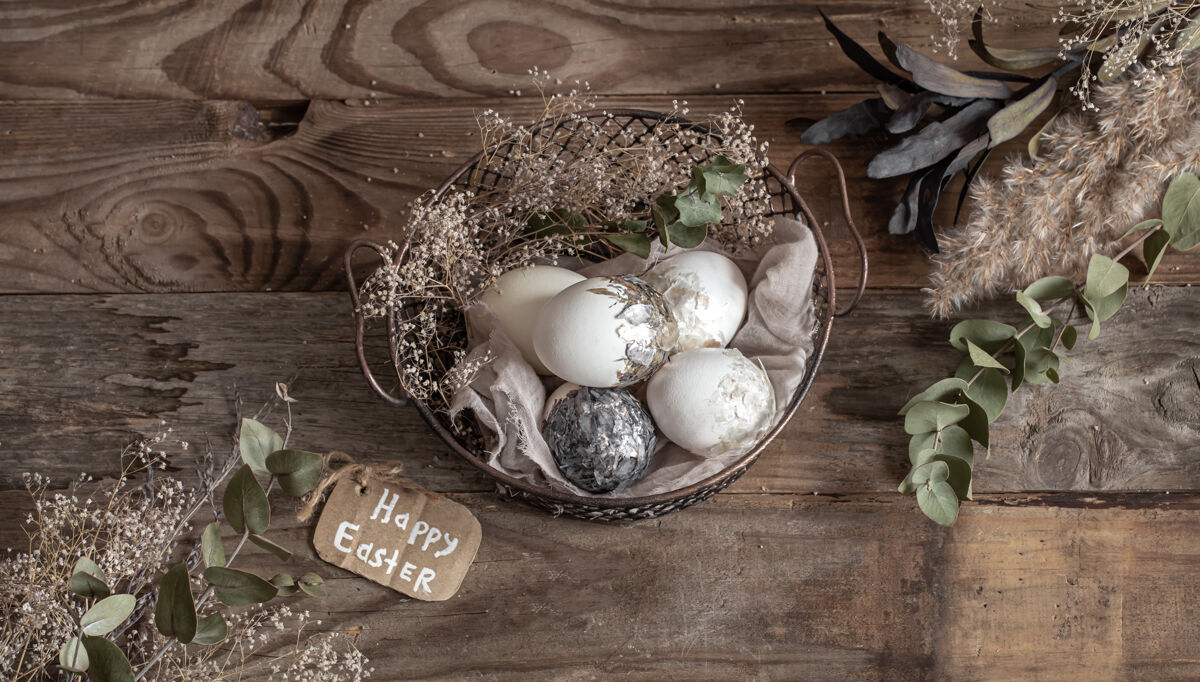 节日复活节彩蛋放在装饰篮子里 木桌上放着干花复活节快乐愿望顶视图铭文