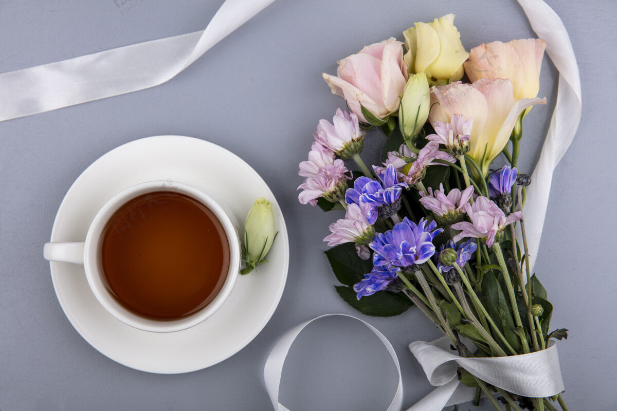 杯子茶碟上的茶杯和灰色背景上带缎带的花朵的俯视图杯子灰色桌子