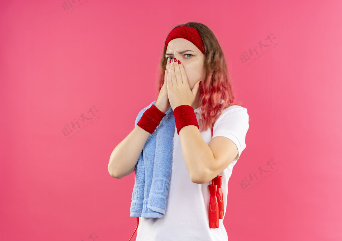 运动戴着头巾 肩上扛着毛巾的年轻运动型女子震惊了 双手捂着嘴站在粉红色的墙上人运动人