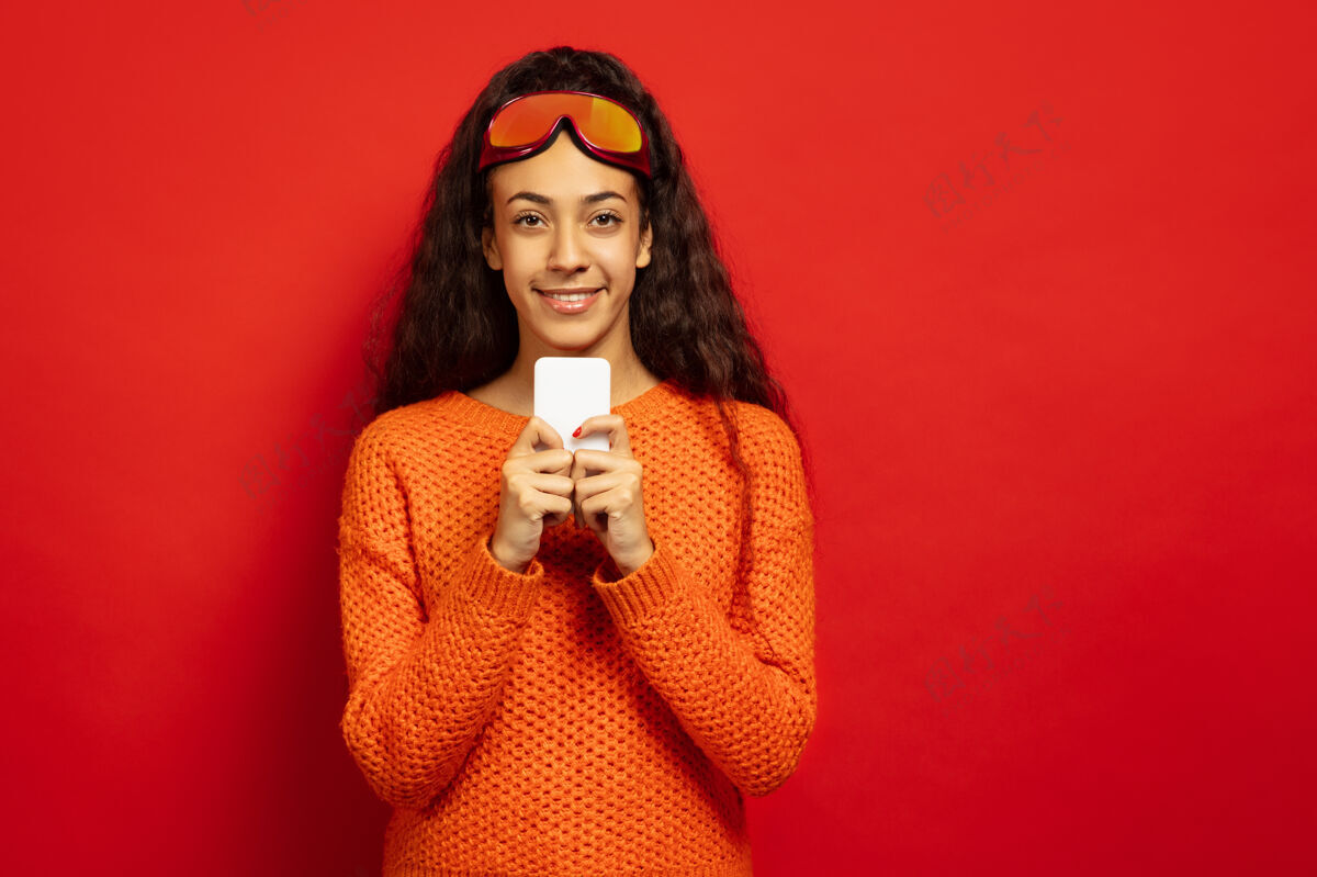 长以红色工作室为背景 黑色皮肤的非洲裔年轻女子的滑雪面具肖像人类情感的概念 面部表情 销售 广告 冬季运动和假期与电话聊天面具黑发运动