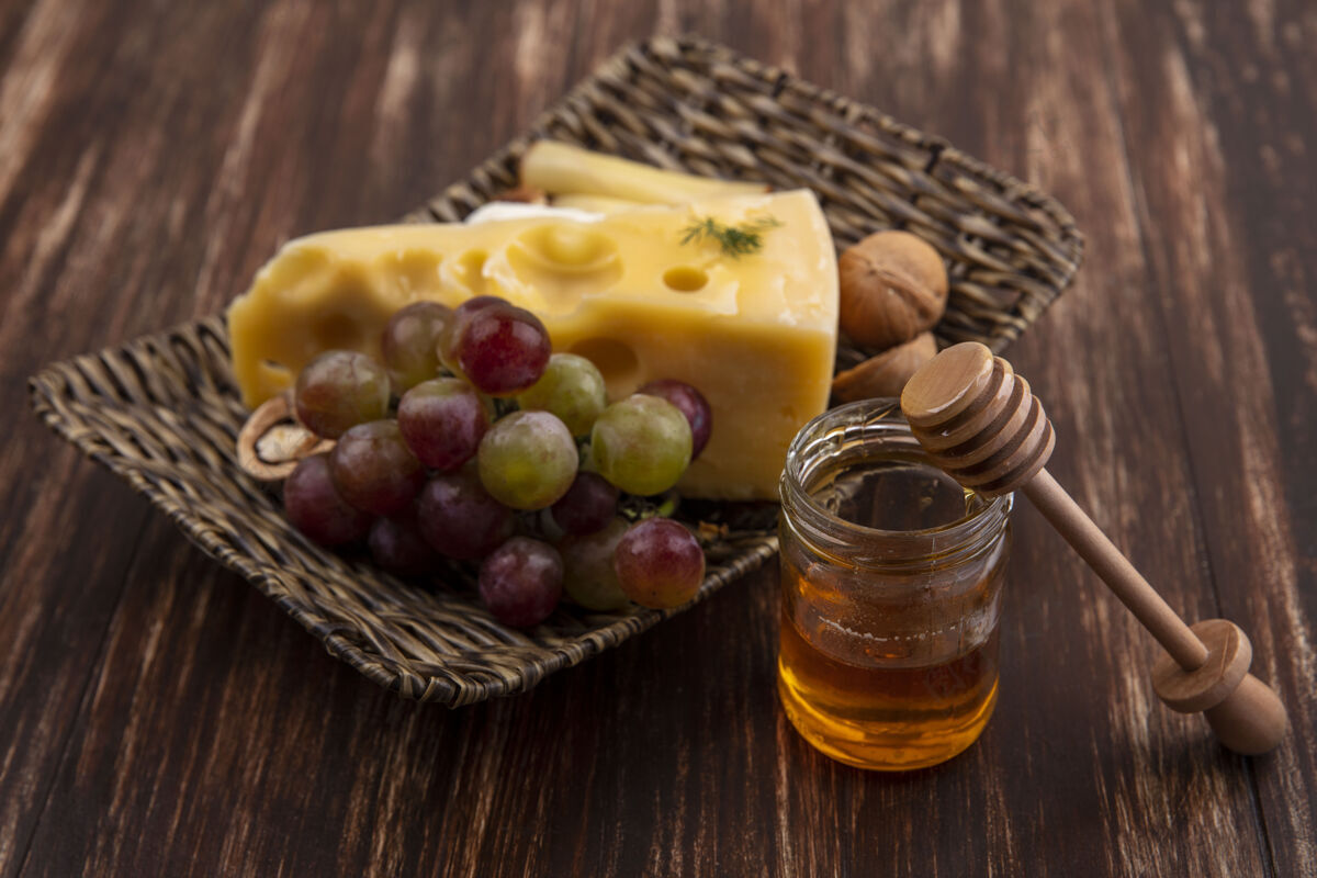 壁板侧视图葡萄与各种奶酪和坚果的立场与蜂蜜在一个木桶的背景支架品种景观