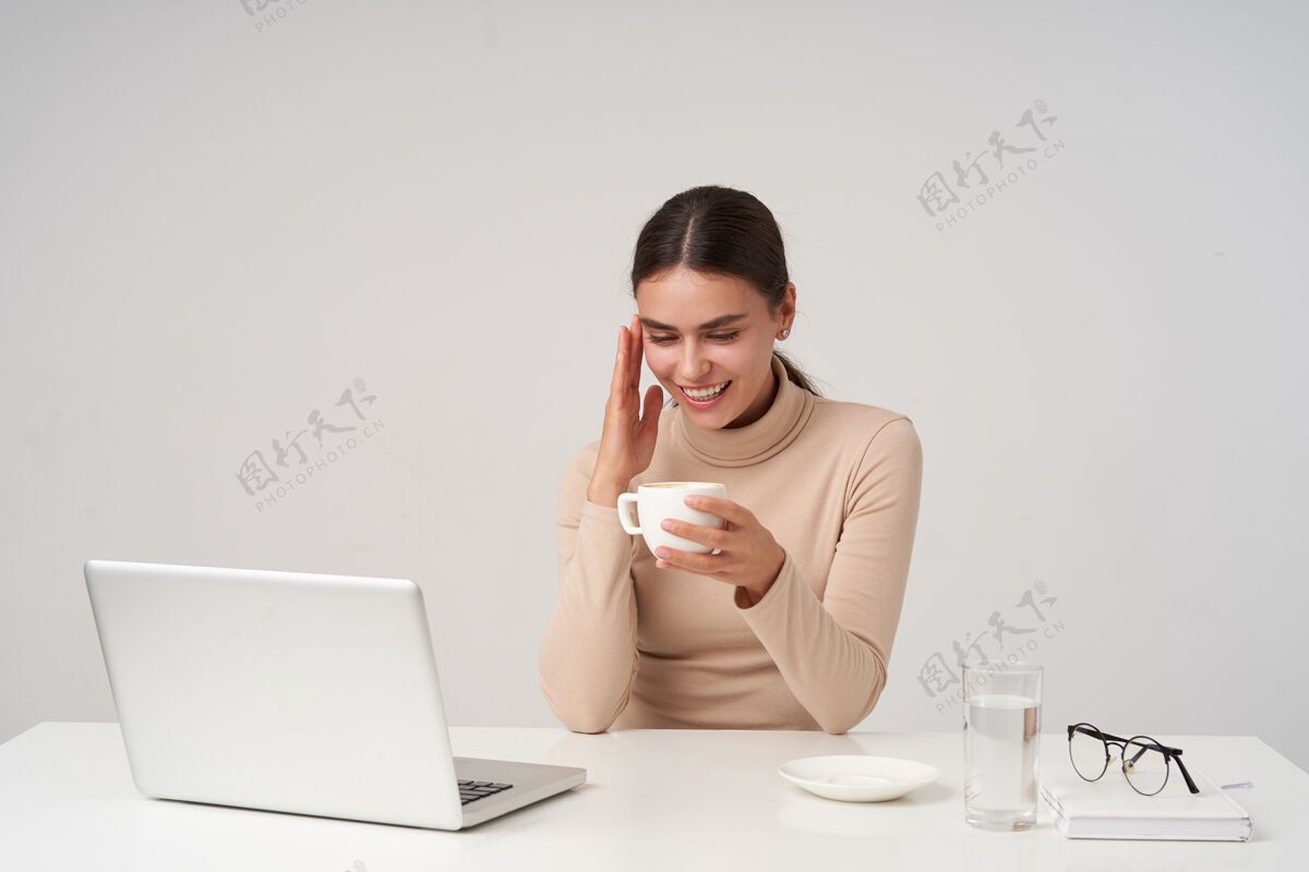 欧洲年轻可爱的黑发女士一边喝着咖啡一边休息 愉快地度过了美好的一天 面带微笑 坐在白墙上的现代办公室里发型模特商务女性