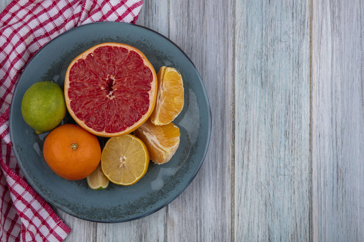酸橙顶视图复制空间葡萄柚一半与橙色和柠檬与石灰在一个棋盘上的灰色背景上的格子毛巾复制橘子视野