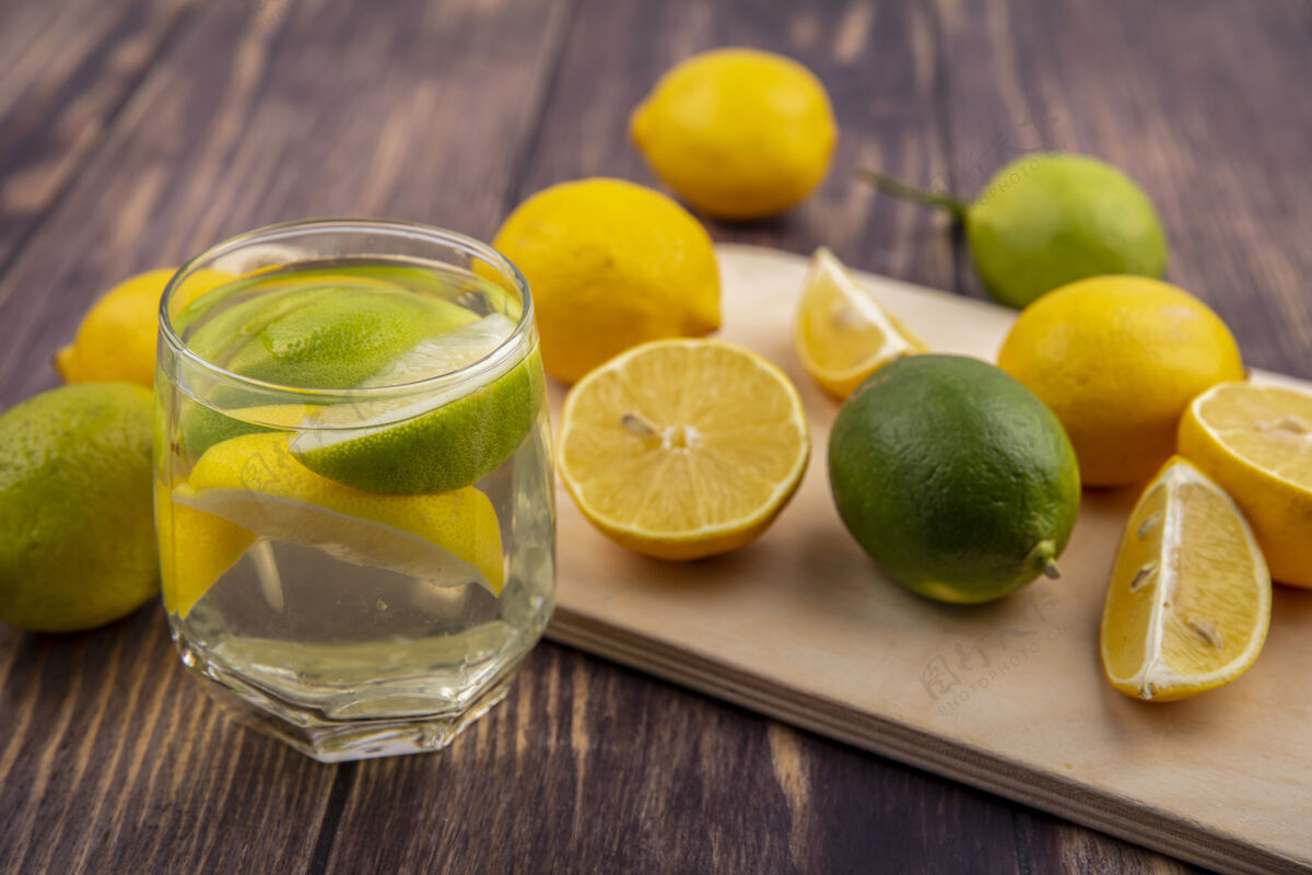 柠檬侧视图柠檬与柠檬在砧板上与一杯排毒水的木制背景玻璃水柑橘