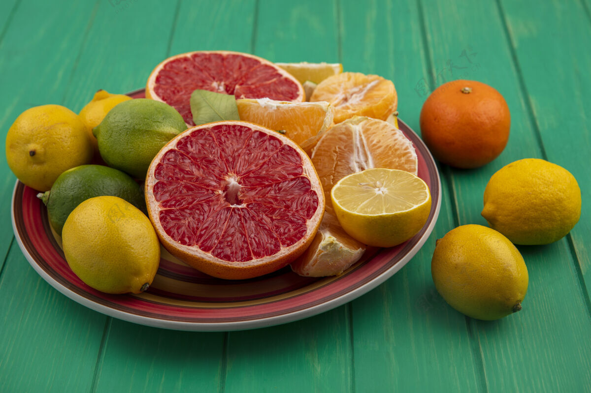 新鲜正面图切半个葡萄柚和去皮的橙子 柠檬和青柠放在一个绿色背景的盘子里酸橙前面切割