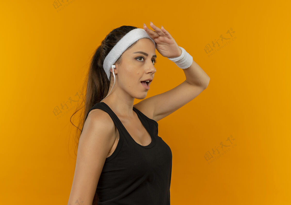 年轻人身穿运动服 头箍 表情自信的年轻健身女士站在橘色的墙上向她致敬靠边站人表情
