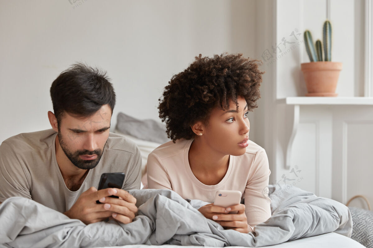 视图图为体贴上瘾的混血男女通过手机应用程序阅读网站 周六上午在床上度过 有技术成瘾夫妇浏览互联网配偶手机家庭