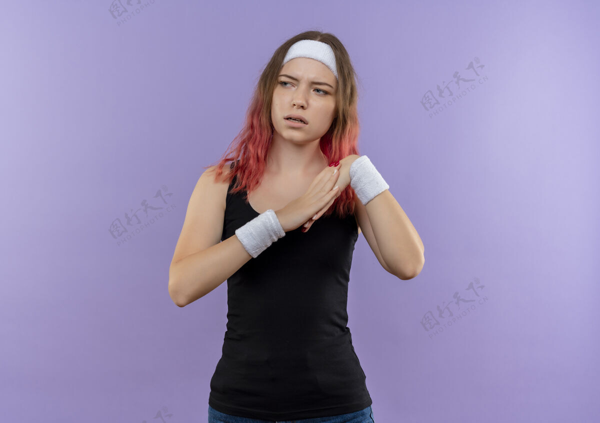 市民穿着运动服的年轻健身女士手牵手一起做热身 严肃的脸站在紫色的墙上看着一边人看着靠边站