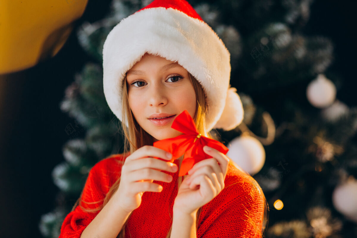 礼物可爱的少女戴着圣诞树旁的红色圣诞帽时尚欢乐圣诞礼物
