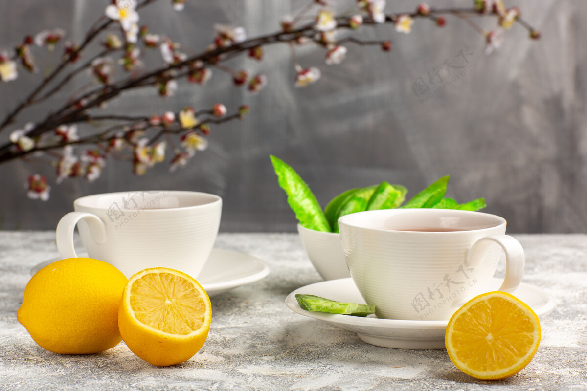 热的前视图：一杯浅白色表面上有柠檬的茶饮料混合饮料茶碟