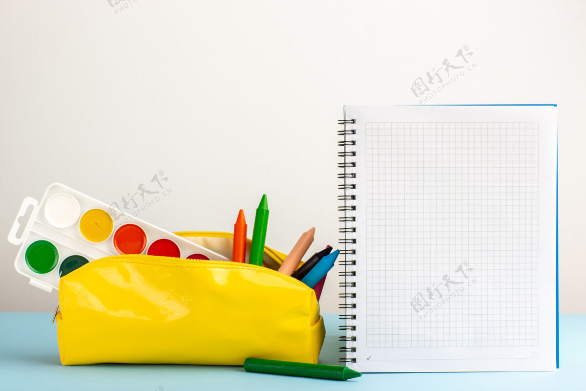彩色正面图蓝色书桌上的黄色笔盒内有不同颜色的铅笔和复写本抄写本钢笔物体