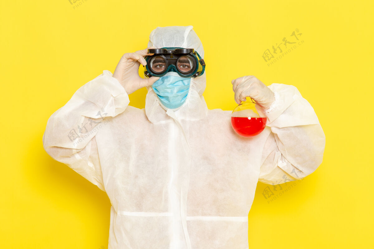 正面正面图穿着特殊防护服的男科学工作者拿着浅黄色表面上有红色溶液的烧瓶医生防护罩工人