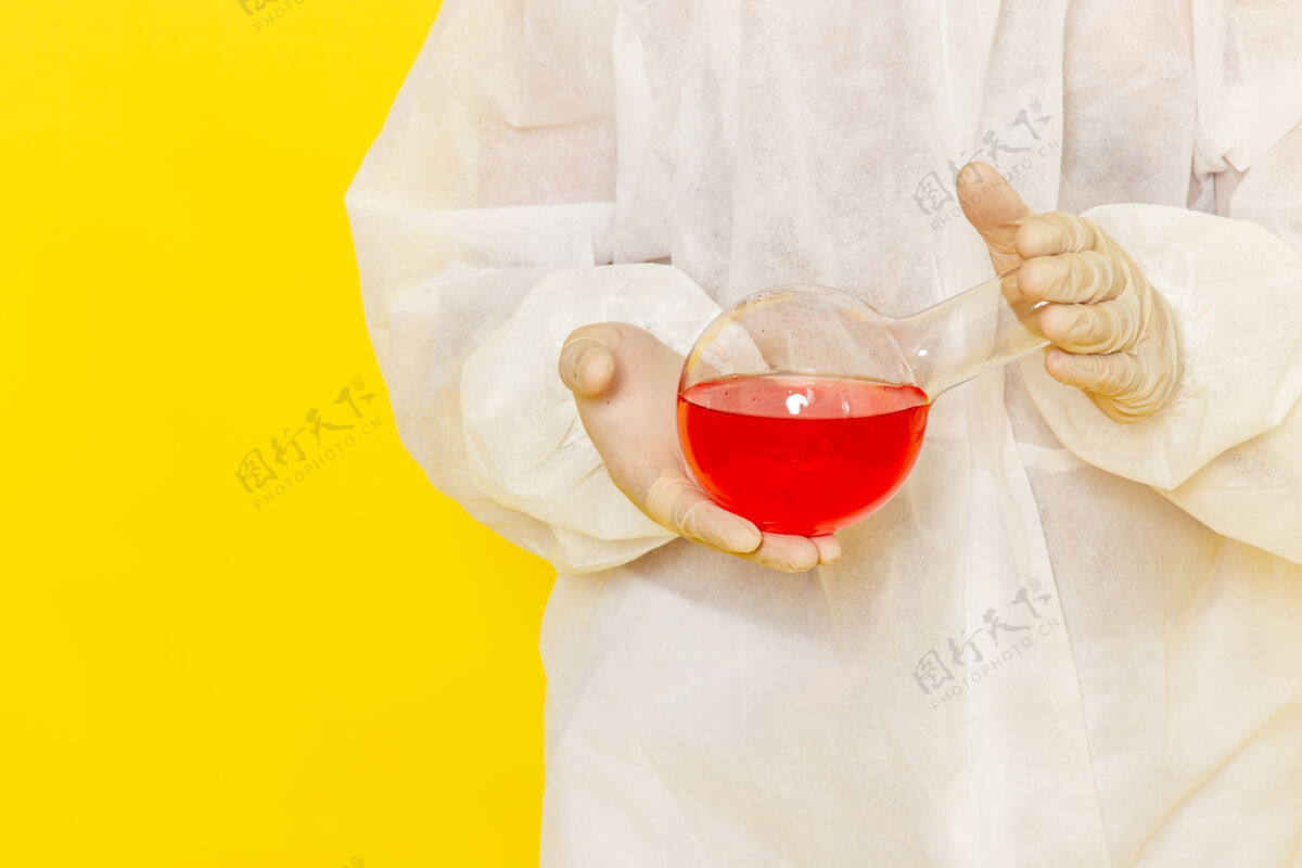 男性正面近距离观察穿着特殊防护服的男性科学工作者 在淡黄色的桌子上拿着装有红色溶液的烧瓶正面特殊饮料