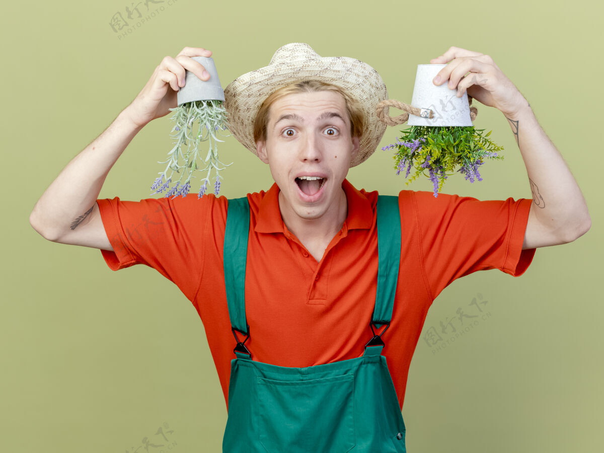 穿年轻的园丁 穿着连体衣 戴着帽子 手里拿着盆栽植物植物年轻相机
