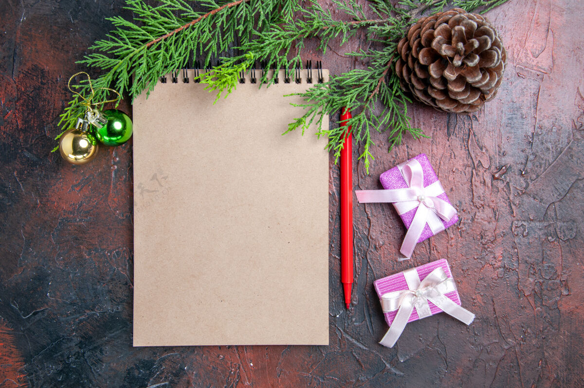 钢笔顶视图红色笔一个记事本松树树枝圣诞树玩具和礼物松果在暗红色的表面记事本松树相册