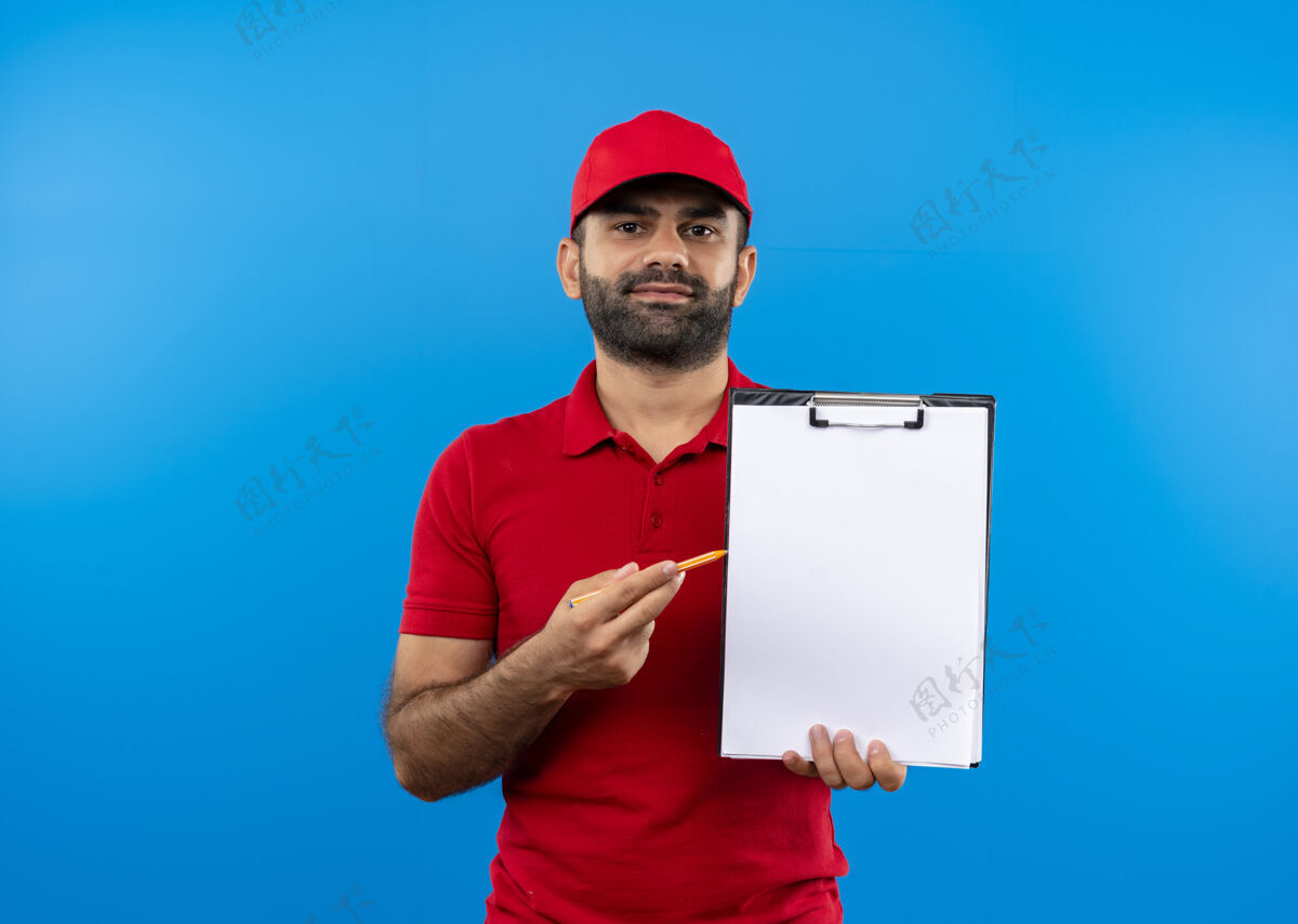 签名一个留着胡须 身穿红色制服 戴着帽子的送货员站在蓝色的墙上 手里拿着一个空白页 要求签名的剪贴板送货制服空白
