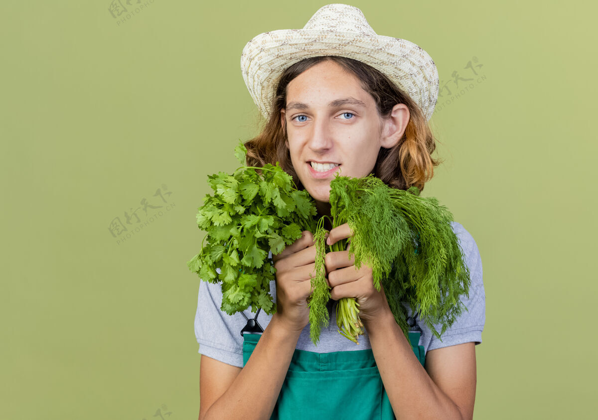 脸年轻的园丁 穿着连体衣 戴着帽子 手里拿着新鲜的草药草药新鲜穿