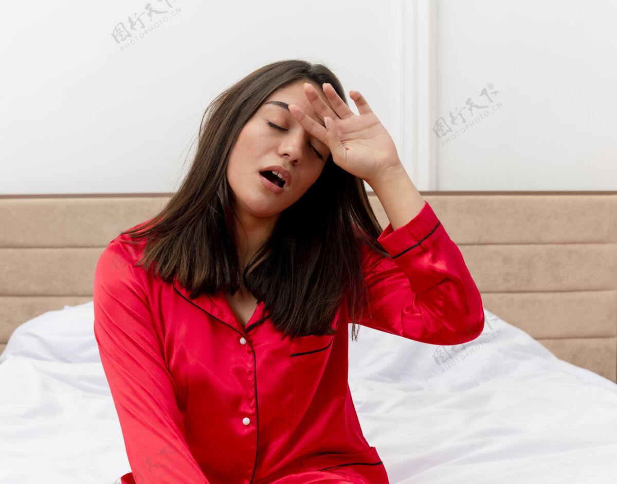 哈欠穿着红色睡衣在床上放松的年轻美女累年轻睡觉