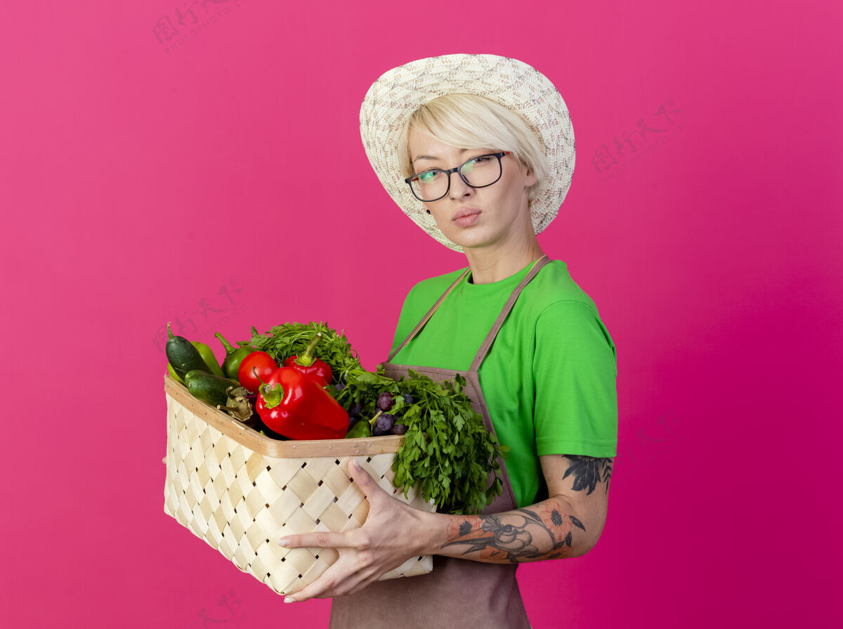 花园一位年轻的园丁 围着围裙 戴着帽子 手里拿着装满蔬菜的箱子脸板条箱短裤