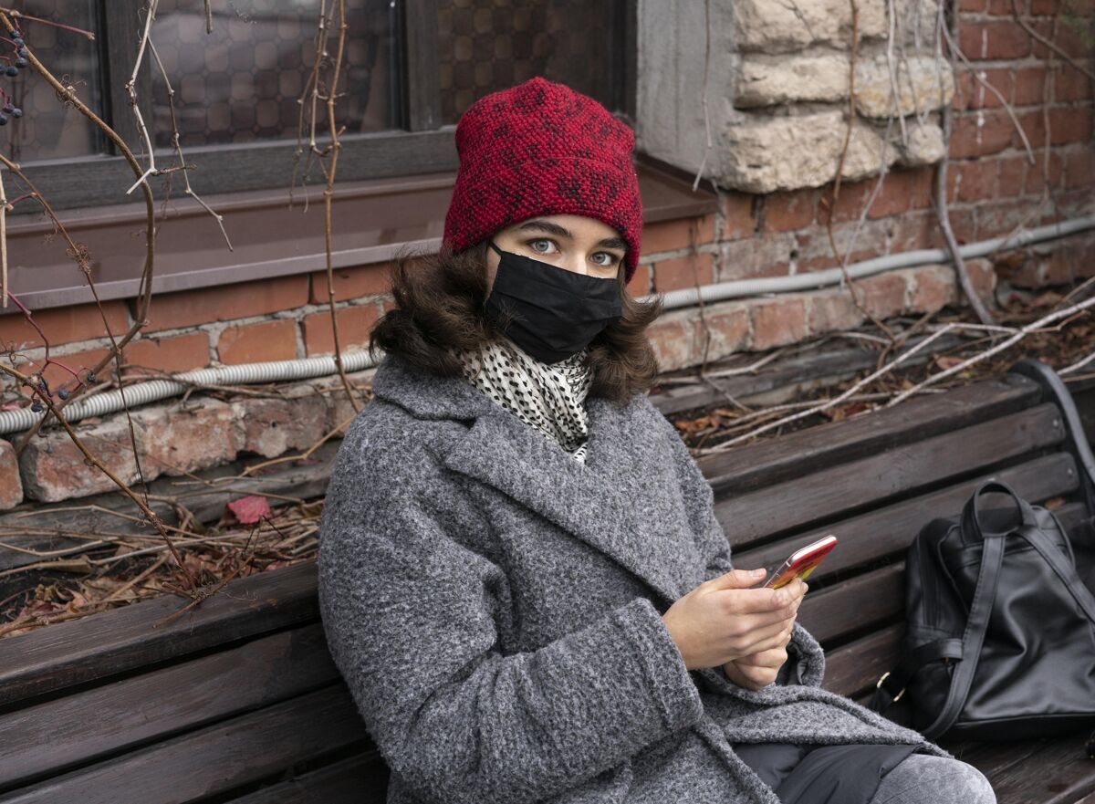公民戴着医用口罩的女人在户外的长凳上用智能手机人女性防护