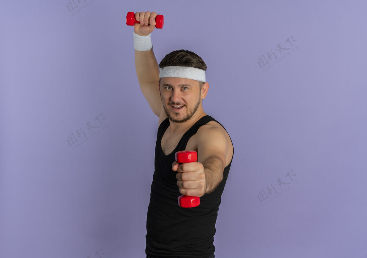 健身戴着头巾的年轻健身男子站在紫色的墙上 带着哑铃 看起来很自信男头带运动装