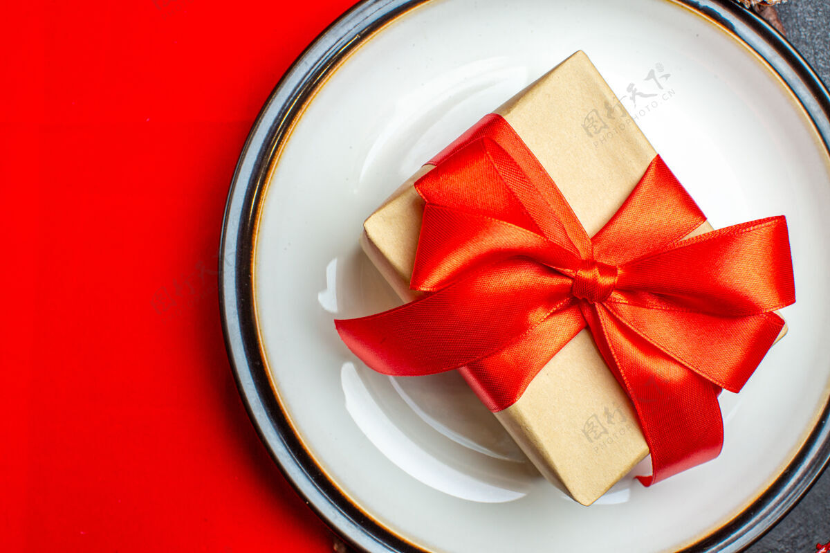 蝴蝶结餐盘上有蝴蝶结形状的礼物 红色餐巾上有缎带 背景为深色餐盘餐巾圣诞节