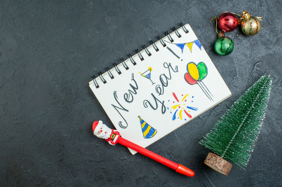 螺旋笔记本上图为黑色背景上的螺旋形笔记本 旁边是圣诞树装饰配件 上面有新年文字和钢笔书写教育颜色