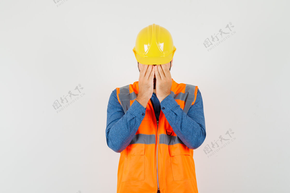 人年轻的建筑工人穿着衬衫 背心 戴着头盔 双手捂着脸 看上去很沮丧 正对着窗外工业背心封面