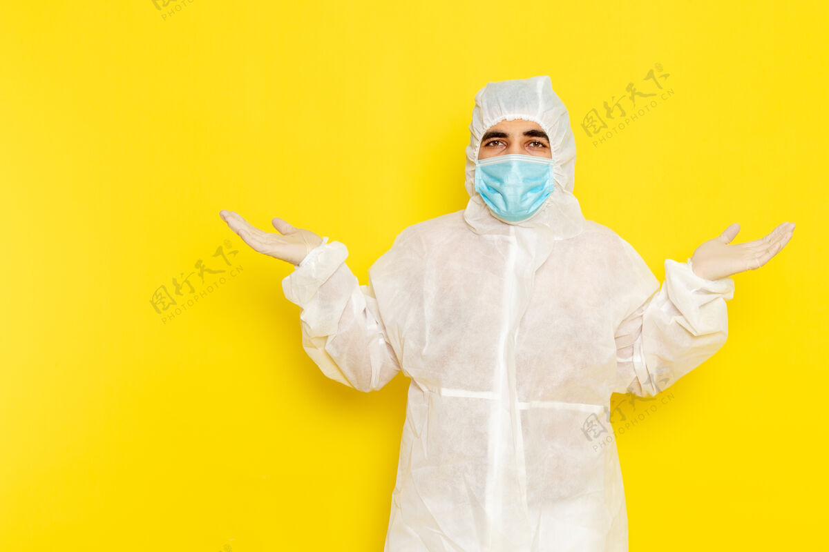 防护身穿白色特殊防护服 黄色墙壁上带无菌口罩的男性科学工作者的正面图危险肖像实验室外套