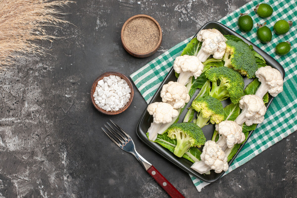 盐顶视图生西兰花和花椰菜在黑色矩形板上绿色和白色方格餐巾纸叉海盐胡椒粉在黑暗的表面自由空间叉子午餐盘子