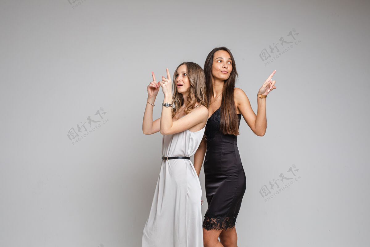 衣服穿着晚礼服的时尚年轻女性 在灰色工作室背景上指向空白处 为您提供内容朋友女士展示