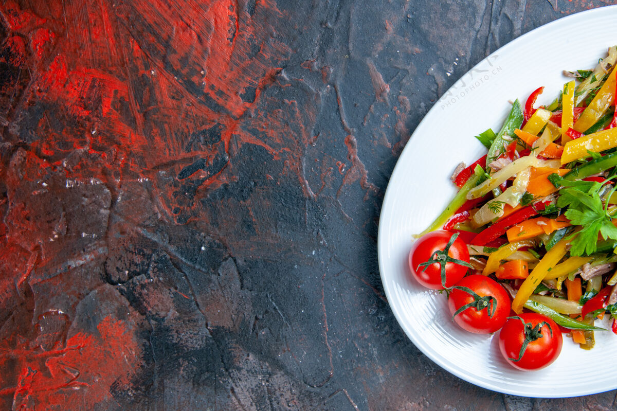 胡椒上半部分查看蔬菜沙拉在椭圆形盘子上暗红色表面的自由空间辣椒辣椒西红柿