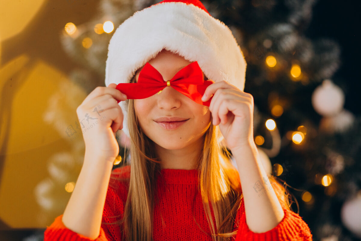 节日可爱的少女戴着圣诞树旁的红色圣诞帽圣诞树圣诞老人可爱