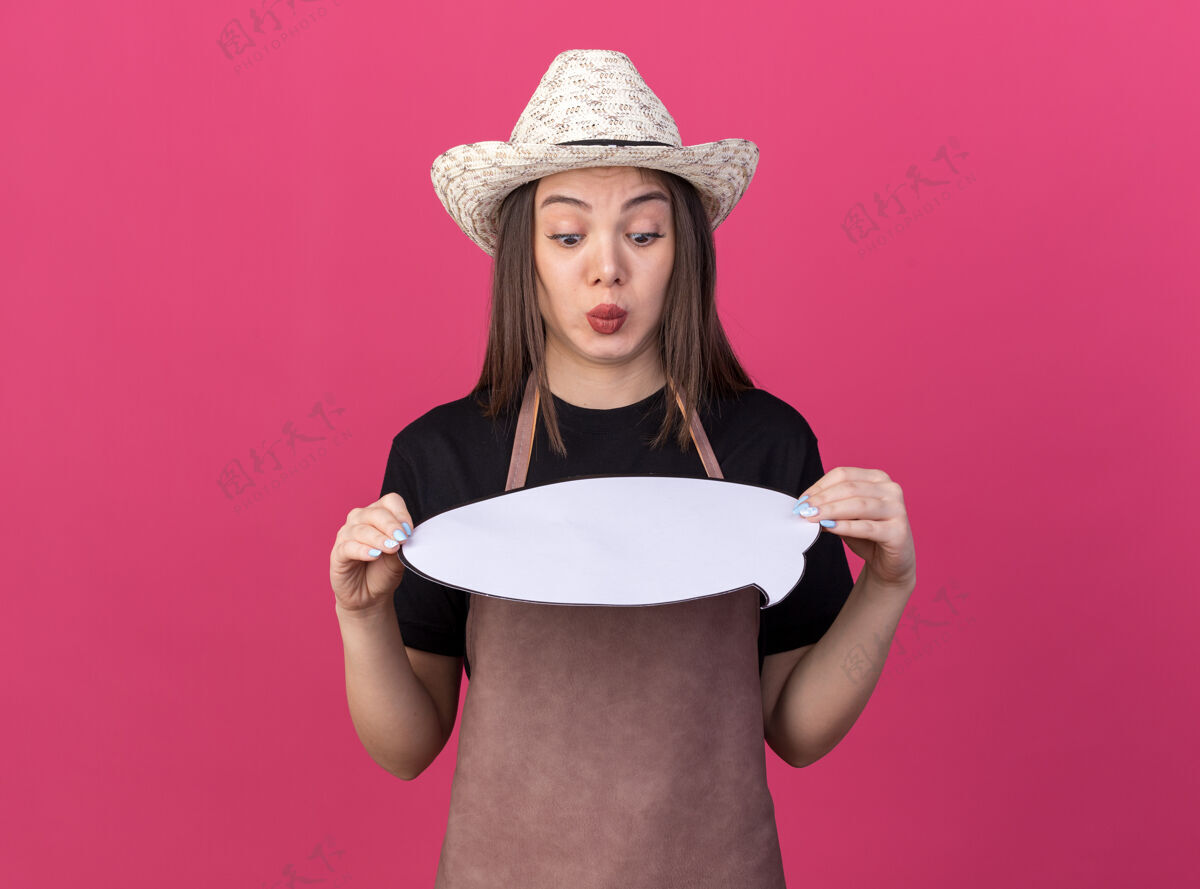 泡泡印象深刻的美丽的白人女园丁戴着园艺帽子拿着 看着粉红色的墙壁上孤立的发言泡沫与复制空间演讲园艺女