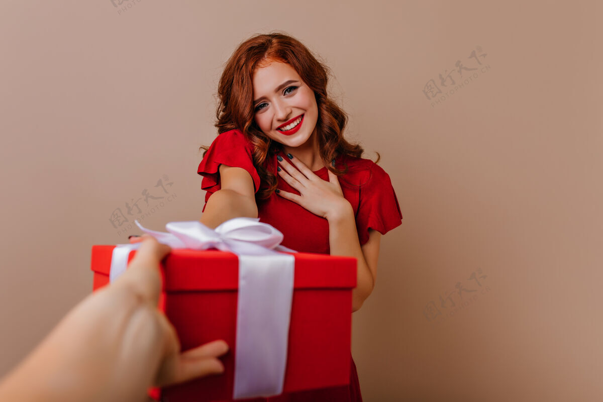 室内羞涩美丽的红衣女孩在她的生日摆姿势室内照片的卷发启发妇女与新年礼物新年聚会积极卷曲