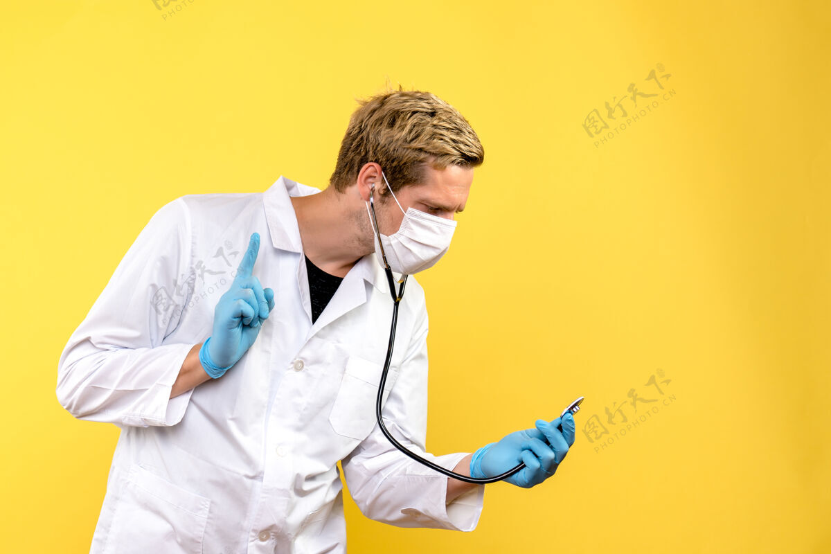 面罩正面图戴着口罩的男医生 黄色桌子上有听诊器外套冠状病毒专业人员