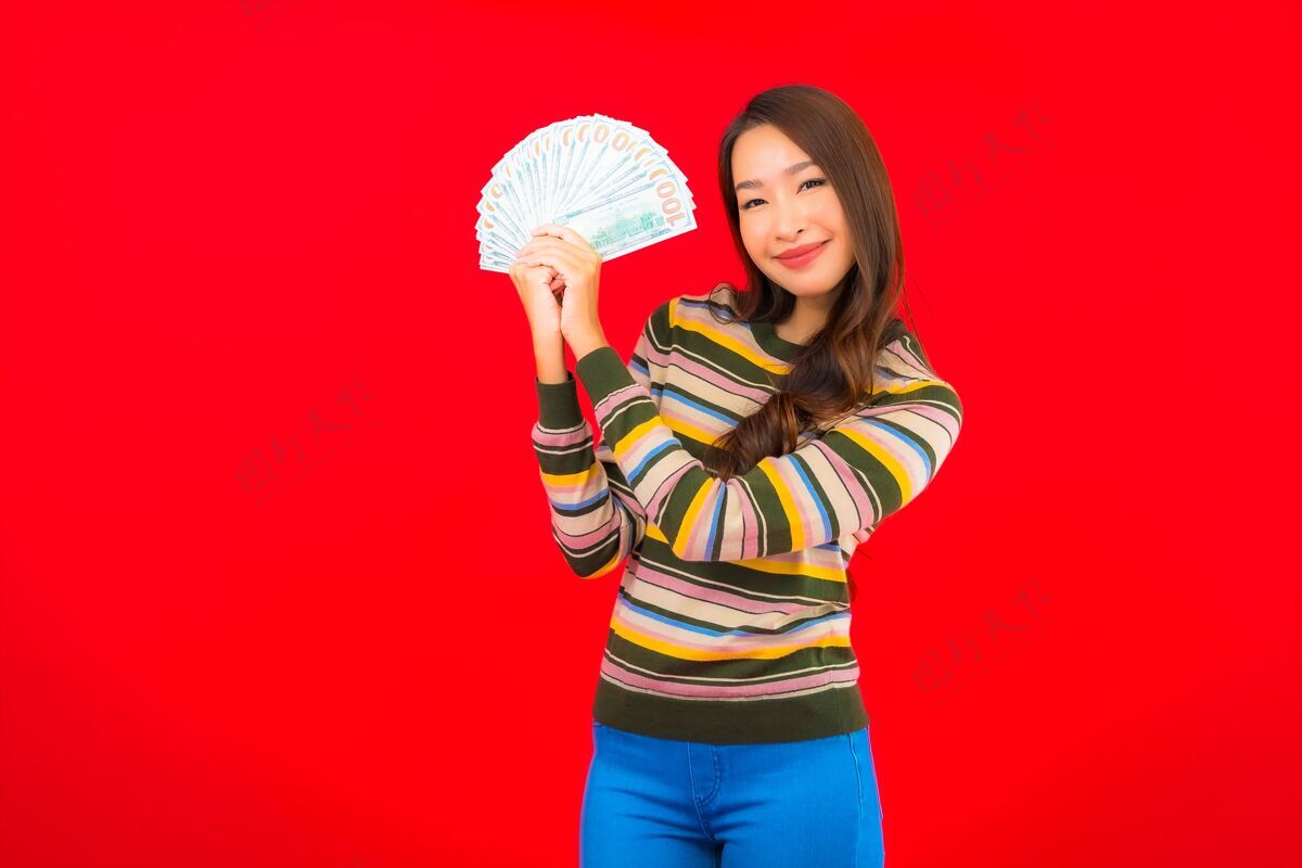 亚洲在红墙上画一幅美丽的亚洲年轻女子的画像 她手里拿着现金和手机货币财富手机