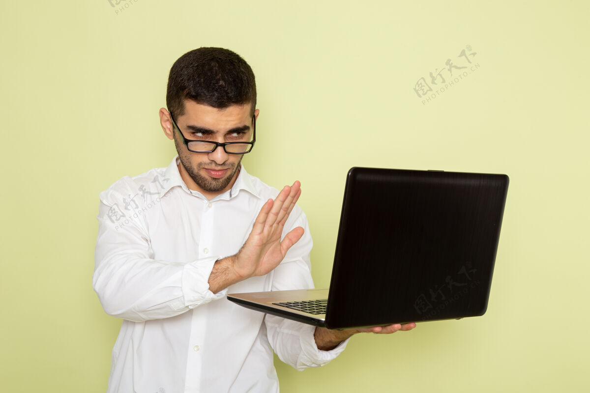 办公室穿着白衬衫的男办公室工作人员在绿墙上使用笔记本电脑的正面视图专业人士便携式便携式电脑