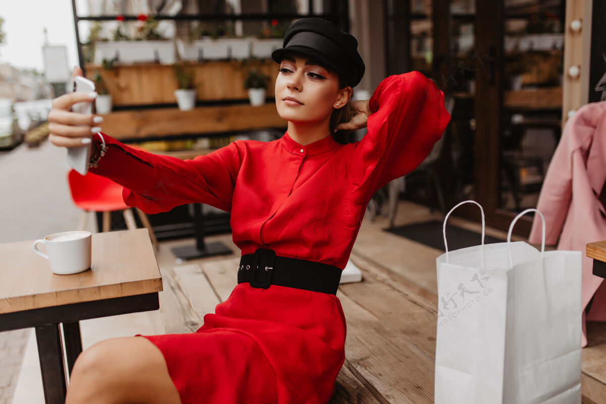法国在清凉的购物之后 这位穿着红色天鹅绒连衣裙 拎着购物袋的年轻女士坐在咖啡馆外 自拍她的新iphone户外教育城市