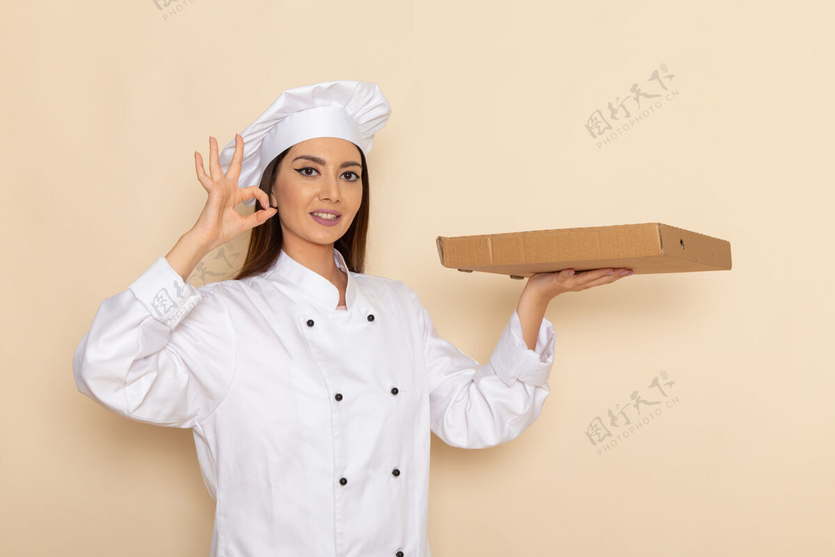 工作身穿白色厨师服的年轻女厨师正拿着食物盒 浅白的墙上挂着微笑专业盒子烹饪