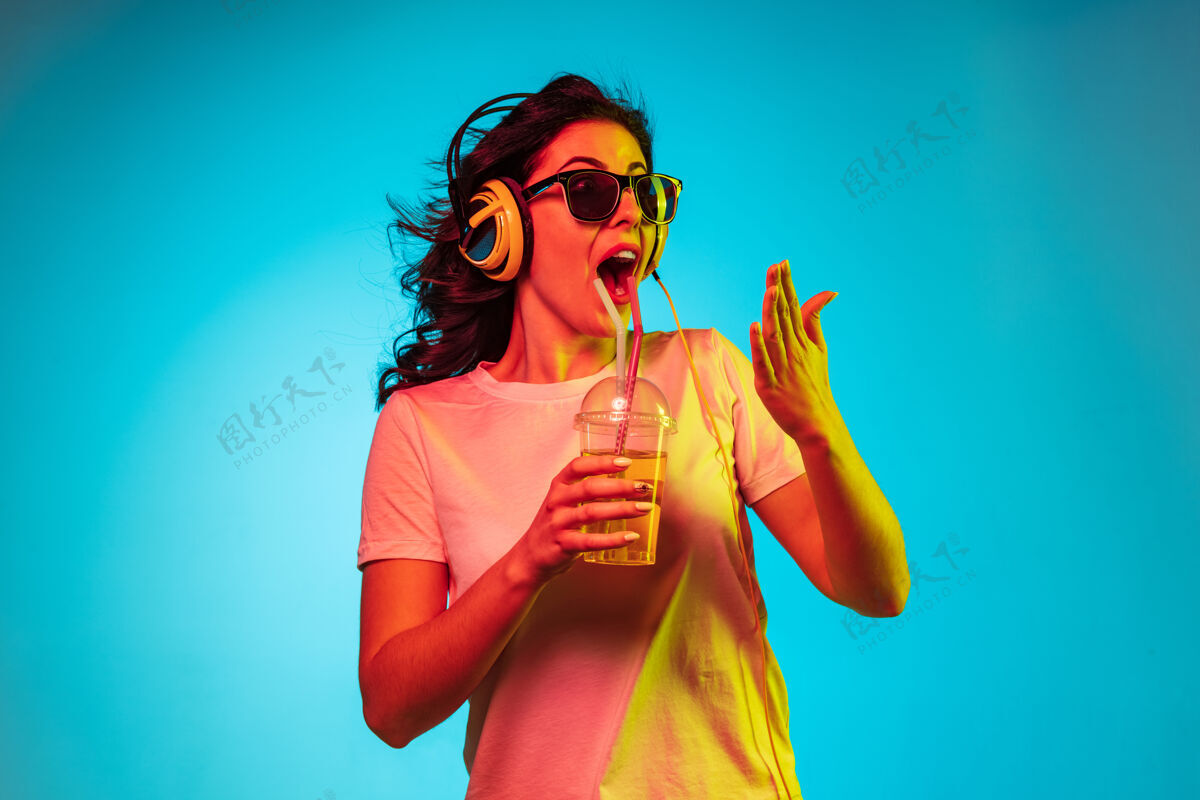 欢快快乐的年轻女子戴着耳机在时髦的蓝色霓虹灯工作室里跳舞和微笑周末情绪海洋