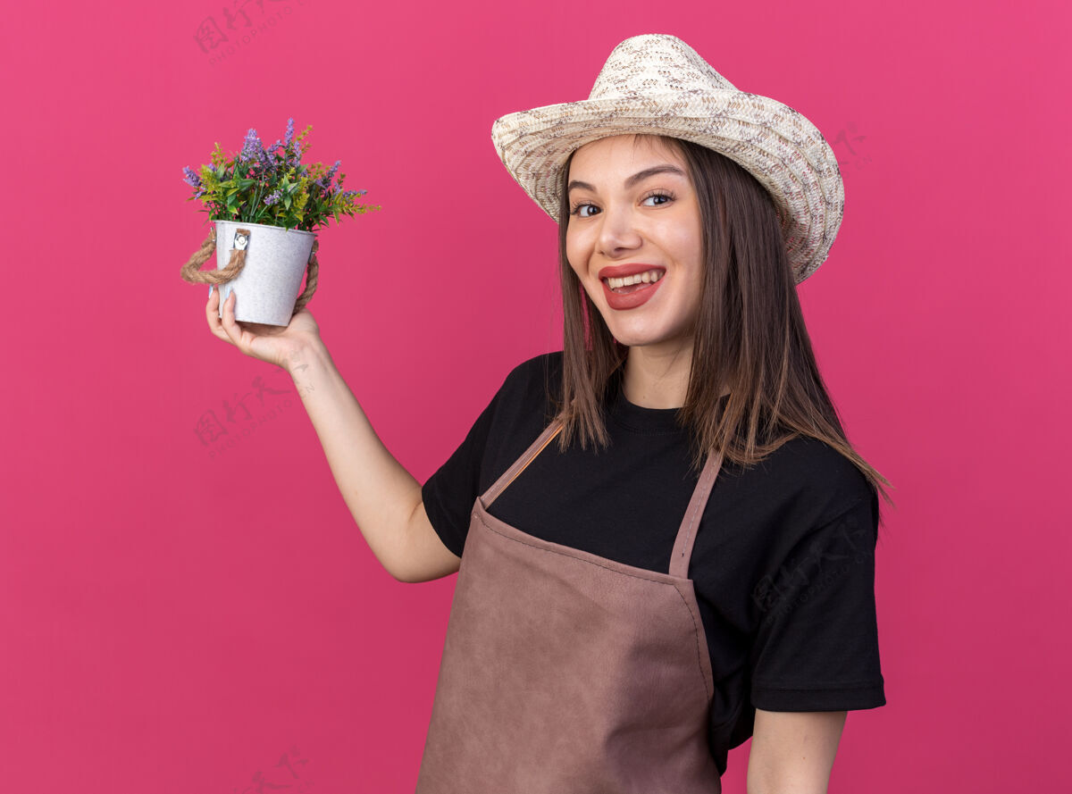 抱笑容可掬的白人女园丁戴着园艺帽 手拿花盆 隔离在粉红色的墙上 留有复制空间微笑花盆花园