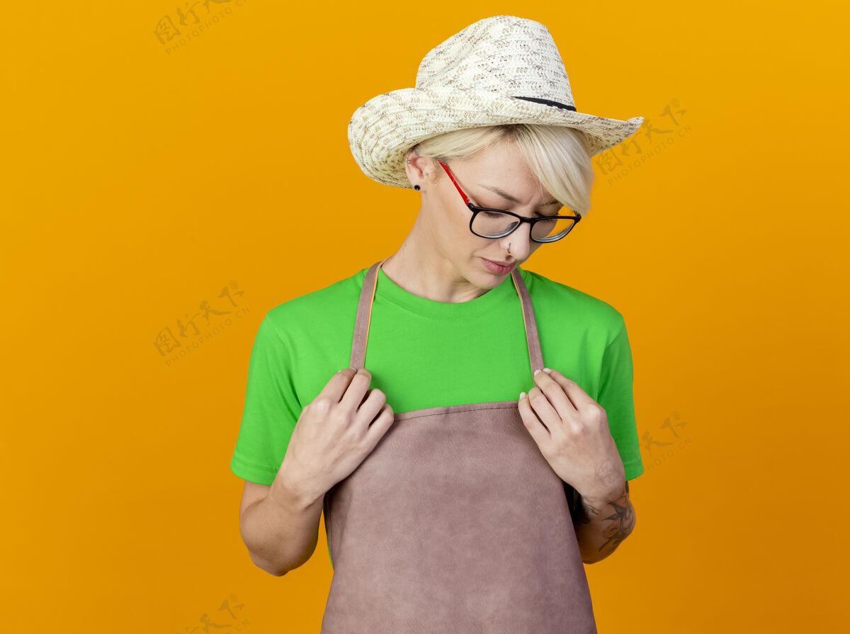 放下一位年轻的园丁 围裙上留着短发 戴着帽子 双手放在胸前 站在橙色的背景上 神情悲伤地往下看表情看橙色