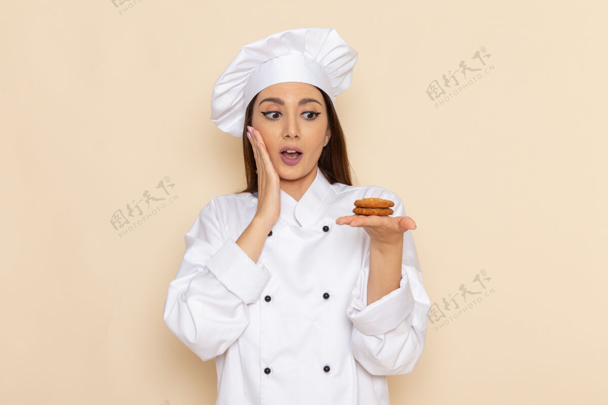 微笑身穿白色厨师服的年轻女厨师正拿着小饼干站在浅白的墙上工作举行女性