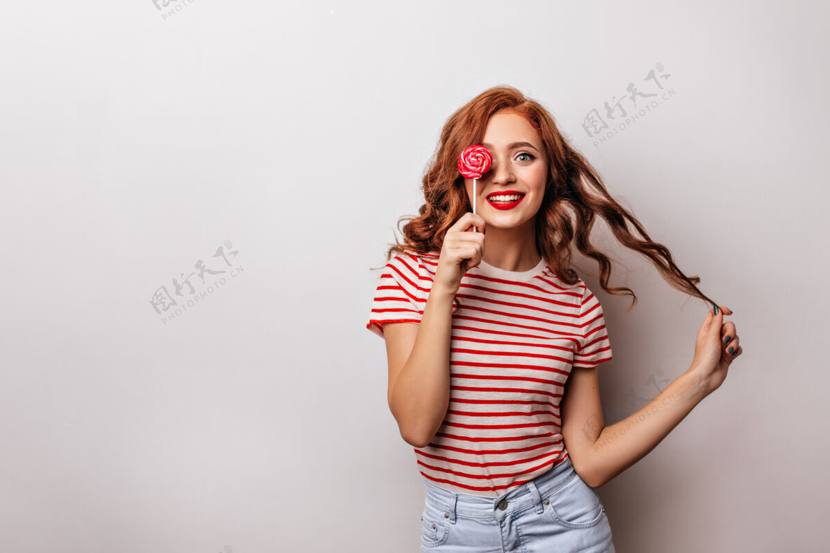 红发有兴趣的白人女孩笑着舔糖果姜味女人配红色棒棒糖表情积极微笑