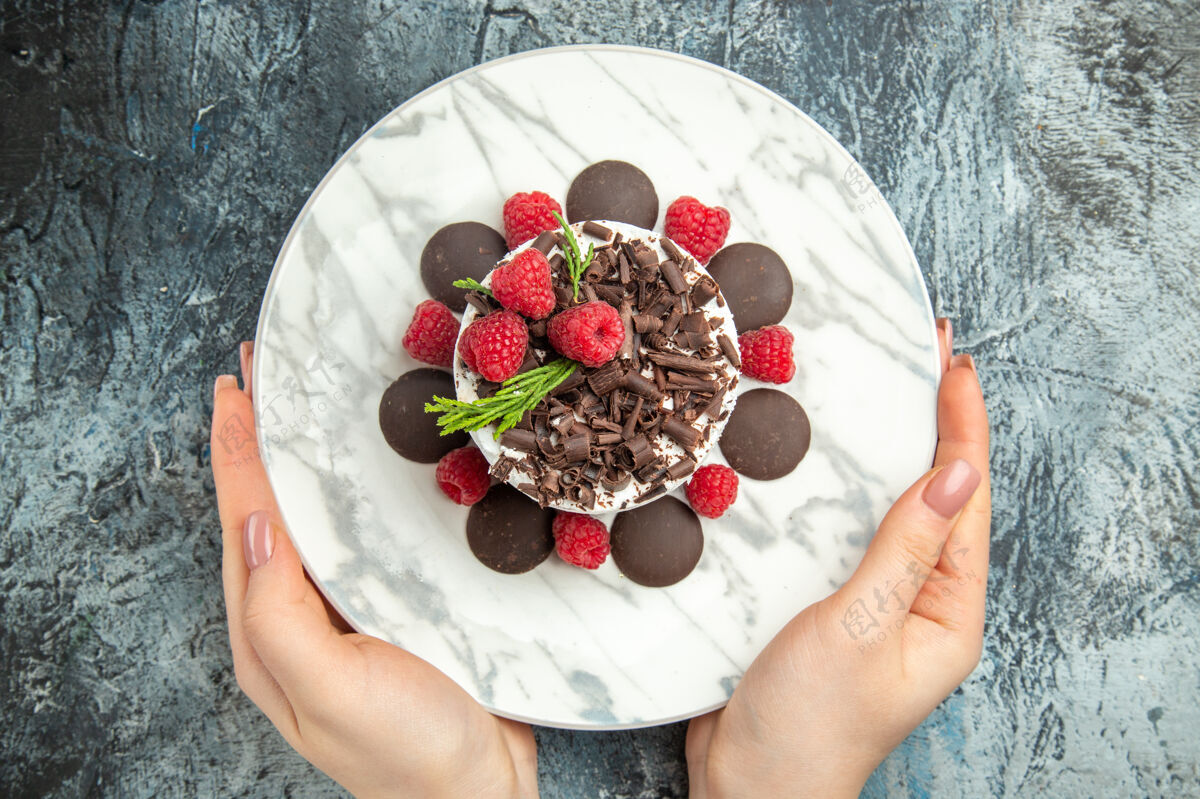 椭圆形俯视图巧克力芝士蛋糕放在椭圆形盘子里 女人手放在灰色的表面上草莓巧克力芝士蛋糕盘子