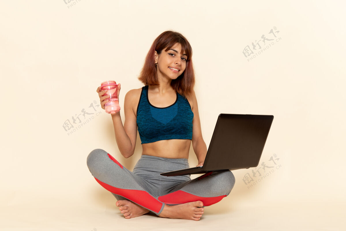 运动年轻女性穿着蓝色衬衫 在浅白的墙上使用笔记本电脑 身体健康锻炼年轻私人教练