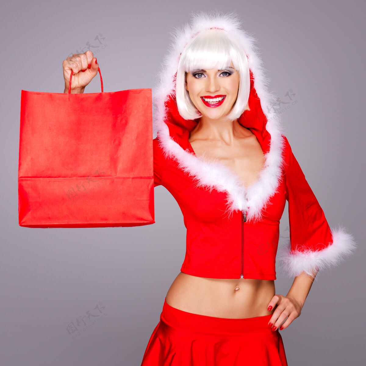 有吸引力穿着雪地少女套装的美丽微笑的女人拿着购物袋举行雪快乐