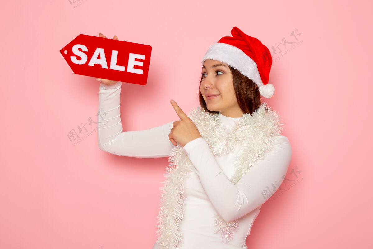 人物正面图年轻女子手持卖写在粉红色墙上的人物彩雪圣诞新年假期时尚美丽年轻女性圣诞