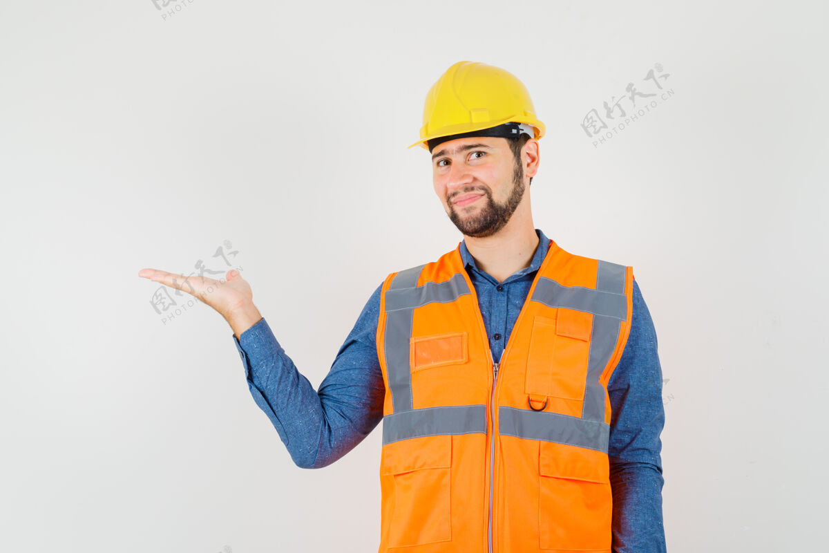 欢呼年轻的建筑工人穿着衬衫 背心 头盔 手掌放在一边 看起来很高兴 正面视图男性工厂工匠